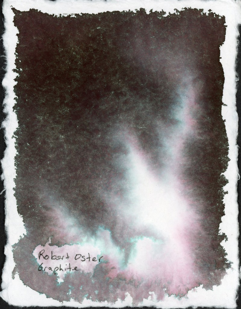 A full page chromatography study on handmade deckle-edge cotton watercolor paper. Robert Oster Graphite floods the page in deep near-black tones with a dramatic teal and pink separation visible throughout. A luminous white and pale pink centre glows through the dark ink. The fibrous texture of the handmade paper creates a wild, unpredictable surface.